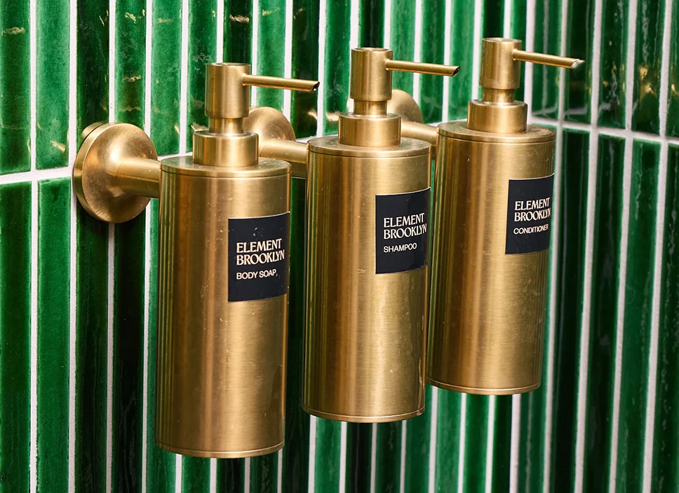 Three brass wall-mounted Element Brooklyn soap dispensers on green tile