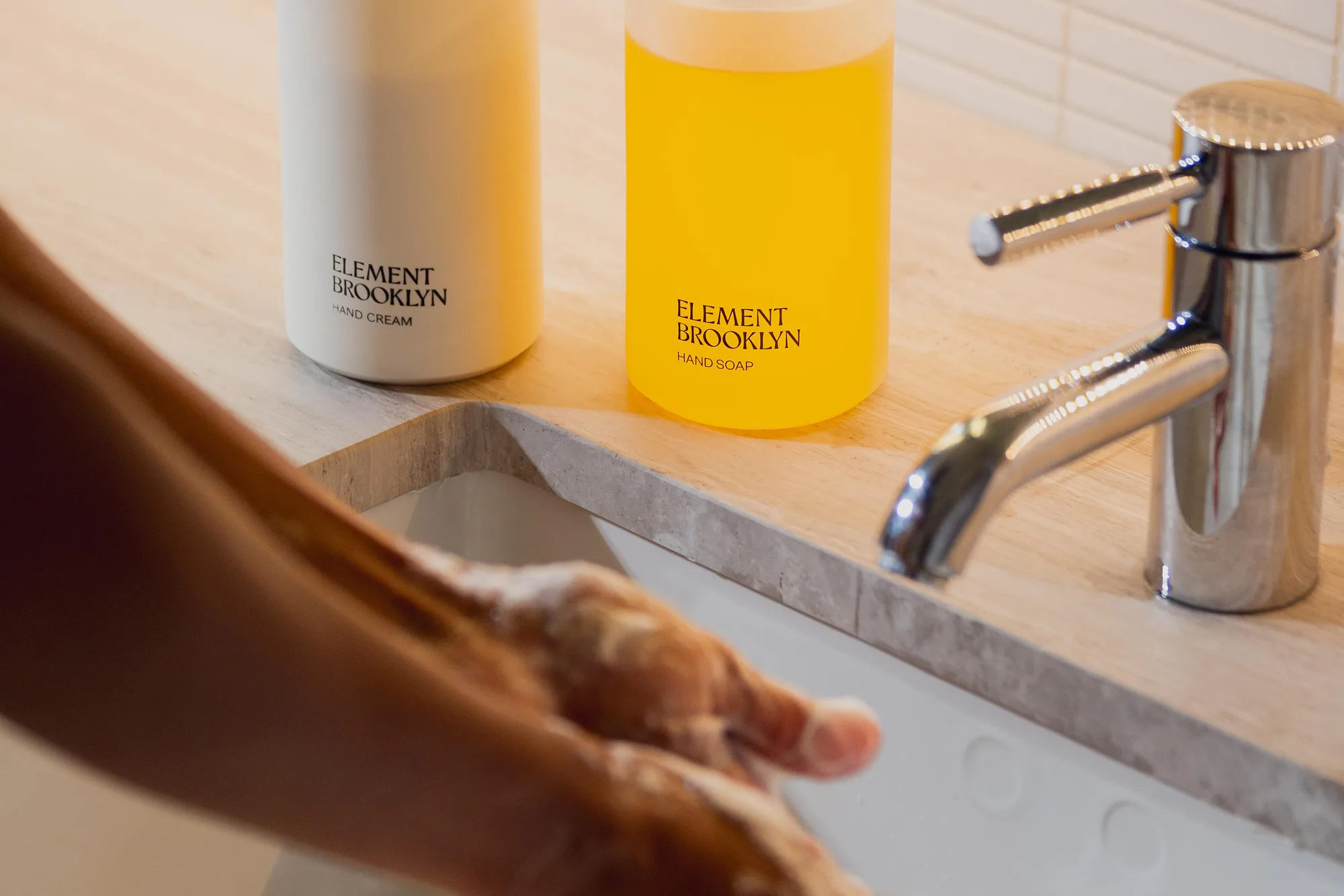 Hands being washed at a sink beside Element Brooklyn soap and hand cream