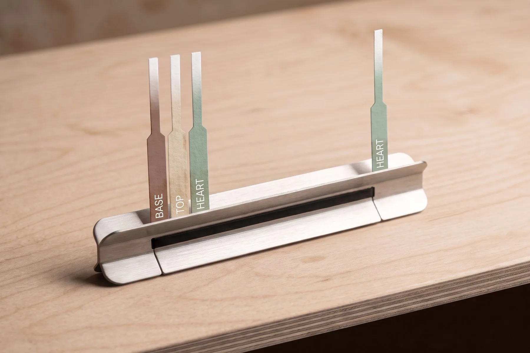 Scent strips labeled Base, Top and Heart in a steel holder on a maple bench