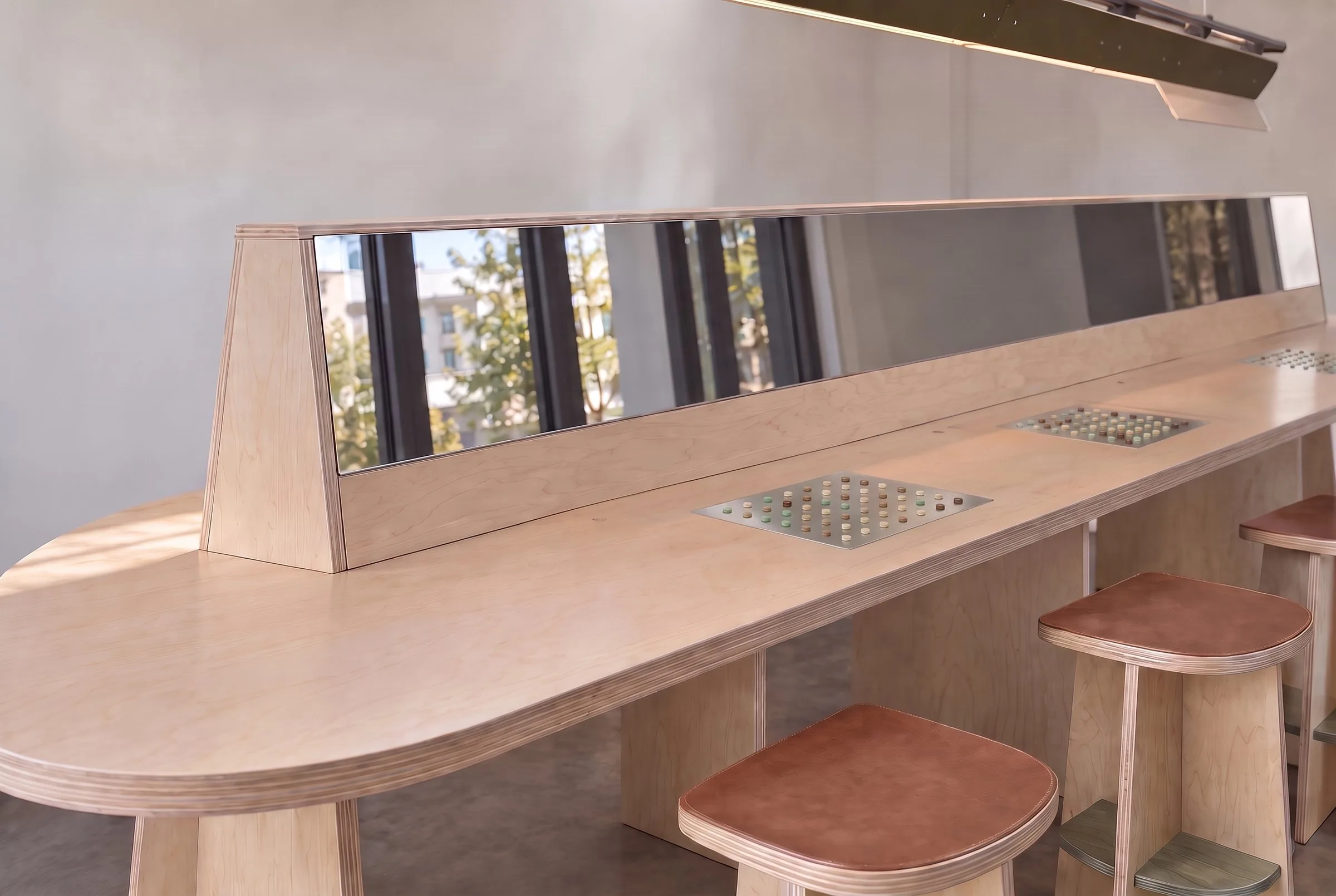 A long maple perfumer’s bench with mirrored screens and stools